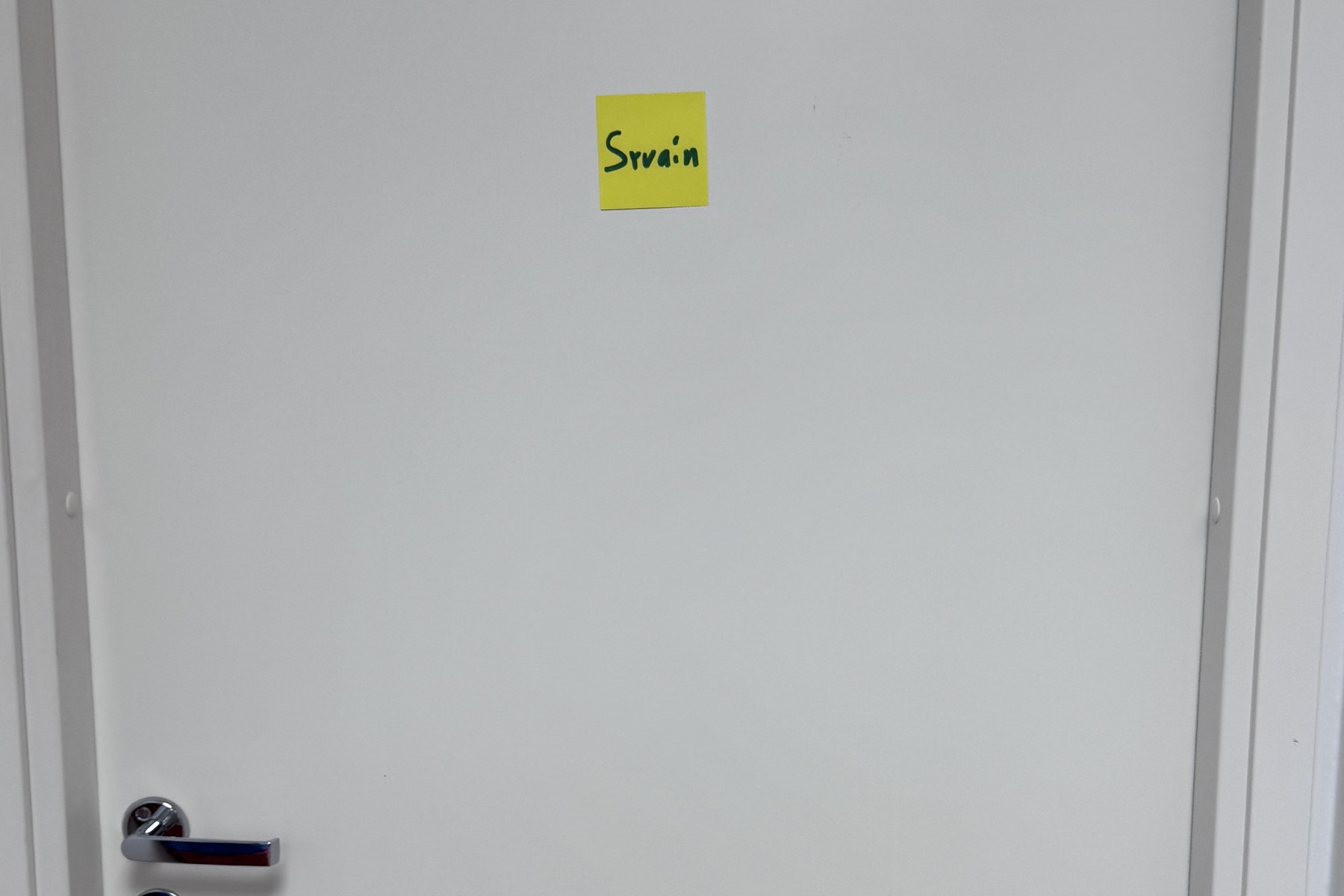 A plain white office door, empty except for a small yellow Post-it note hand-scrawled with our name.